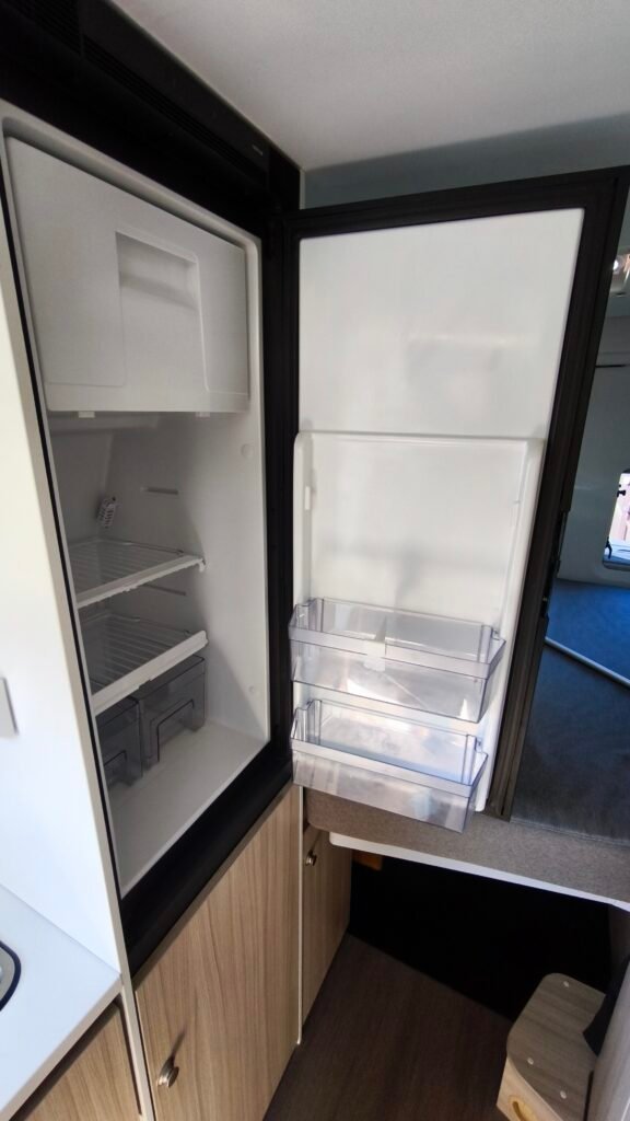 Obrázek interiéru obytného vozu s moderním chladničkou a úložnými prostory. Ideální pro kempování a dobrodružství.