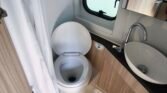 Obrázek interiéru karavanu s toaletou a umyvadlem. Moderní design a funkčnost pro pohodlné cestování.