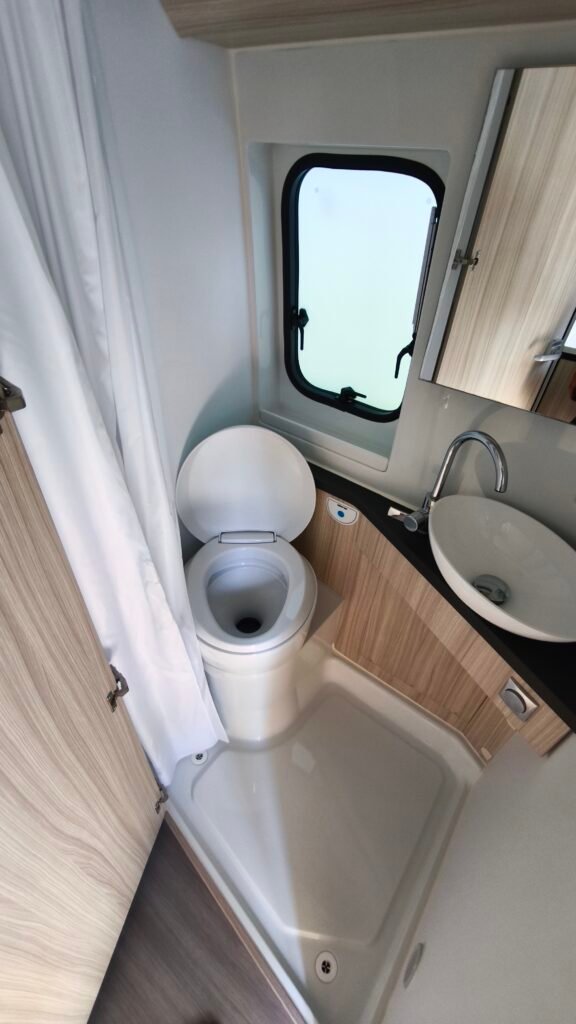 Obrázek interiéru karavanu s toaletou a umyvadlem. Moderní design a funkčnost pro pohodlné cestování.