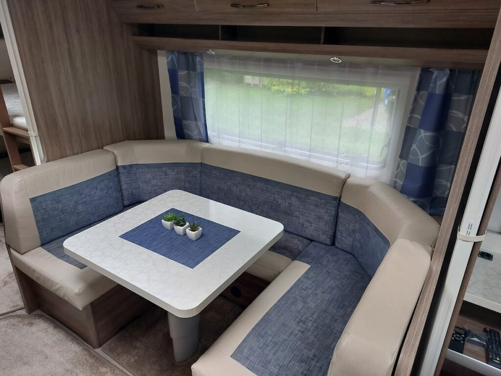 Obrázek interiéru karavanu s pohodlným sezením a stolem. Moderní design pro příjemné cestování.