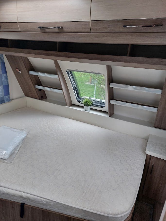 Interiér karavanu s pohodlnou postelí a úložnými prostory. Ideální pro vaše cestování a odpočinek.