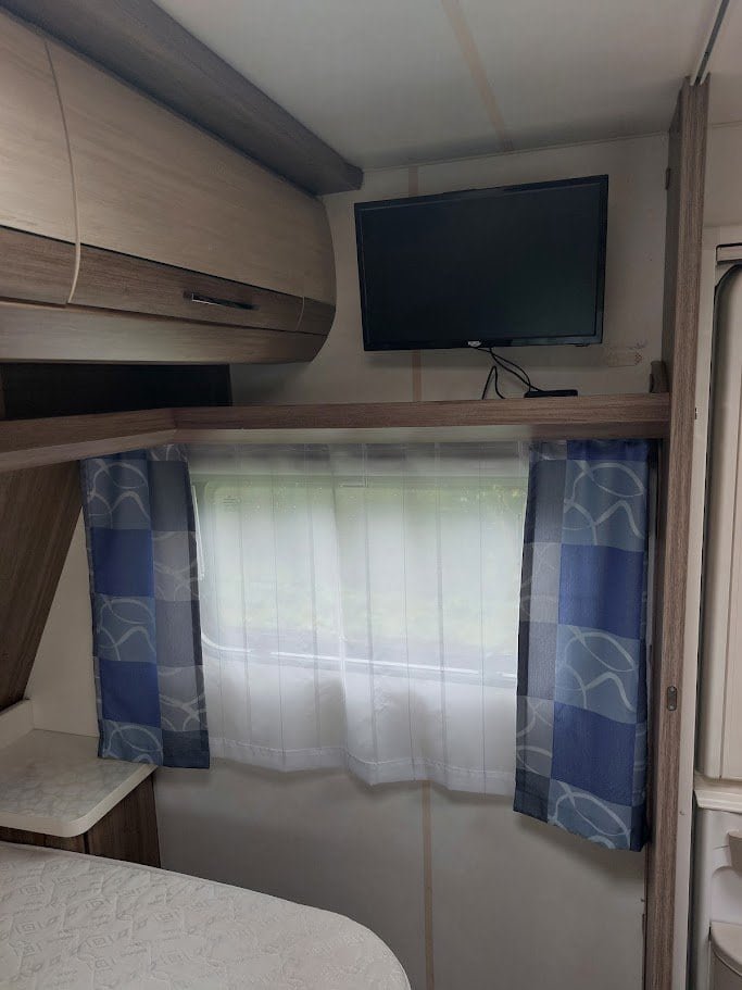 Obývací prostor v karavanu s televizí a záclonami. Vhodný pro relaxaci při cestování.