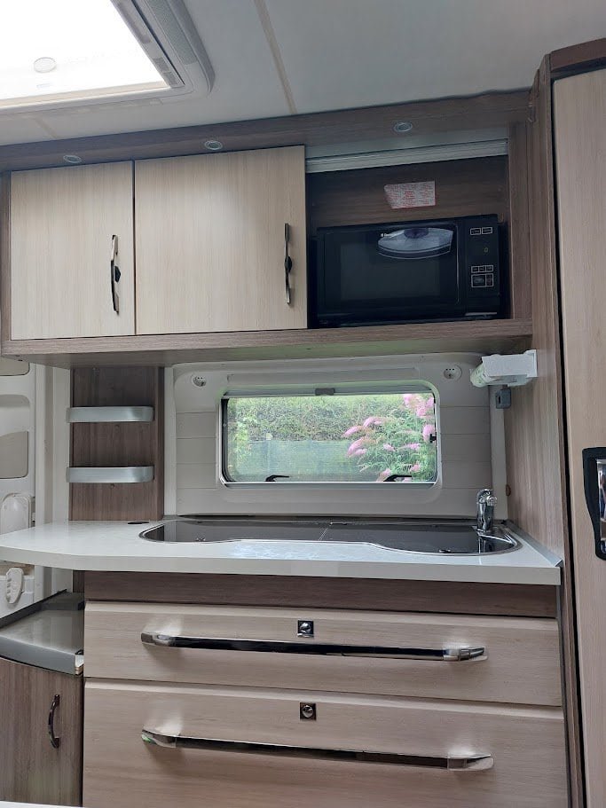 Obrázek interiéru karavanu s moderní kuchyní a mikrovlnnou troubou, ideální pro pohodlné cestování.