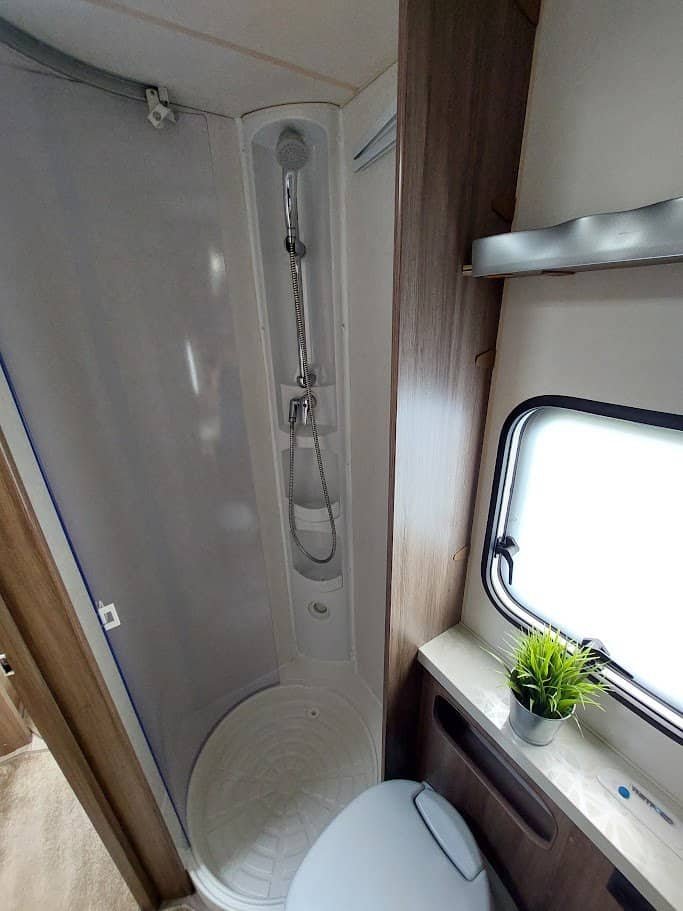 Obrázek interiéru karavanu s moderním sprchovým koutem a toaletou. Praktický design pro pohodlné cestování.