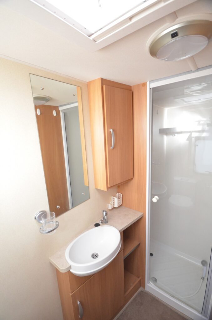Moderní koupelna v karavanu, s umyvadlem, skříňkami a sprchovým koutem. Komfortní a praktické vybavení pro cestování.