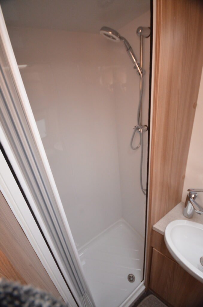 Obrázek zobrazuje sprchový kout v obytném autě s jednoduchým designem a dřevěnými prvky.