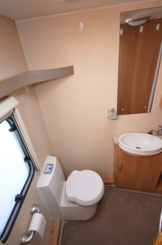 Obrázek zobrazuje koupelnu v karavanu s umyvadlem a toaletou, ideální pro pohodlné kempování.