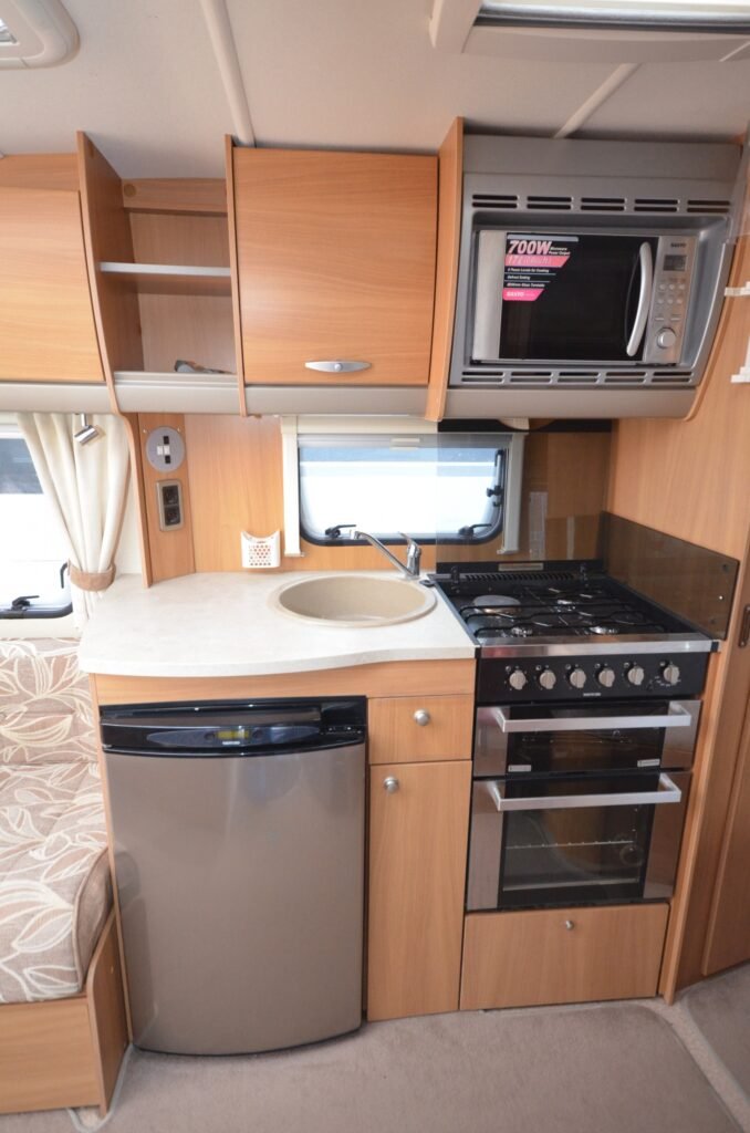 Interiér obytného vozu s moderní kuchyňkou, sporákem, mikrovlnkou a chladničkou. Ideální pro cestování.