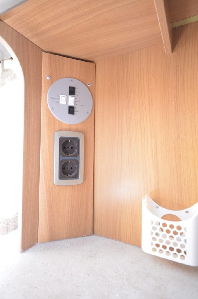 Obrázek znázorňuje interiér obytného vozu s elektrickými zásuvkami a ovládacími prvky.