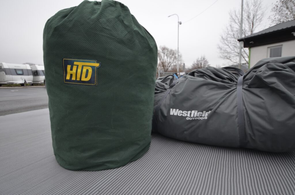 Obrázek zobrazuje karavany v pozadí s taškami HTD a Westfield Outdoors v popředí. Ideální pro kempování!