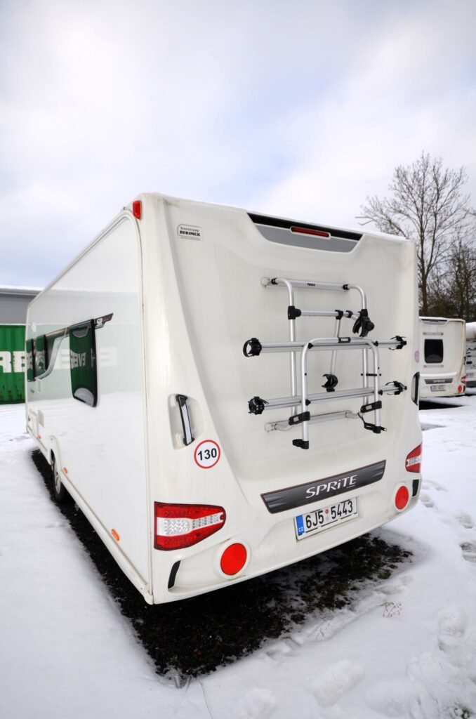 Obytné auto Sprite, bílé, s nosičem kol, připravené na dobrodružství v zimní krajině.