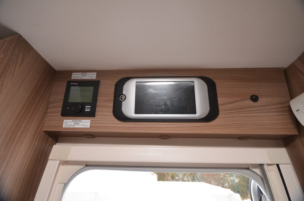 Obrázek ukazuje ovládací panel a displej v interiéru obytného auta, což naznačuje moderní technologii pro pohodlné cestování.