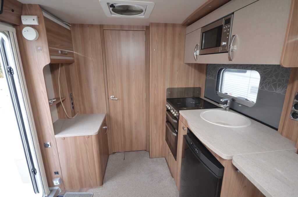 Obrázek interiéru obytného auta s moderním zařízením a dřevěnými prvky. Funkční kuchyňka a pohodlný prostor.