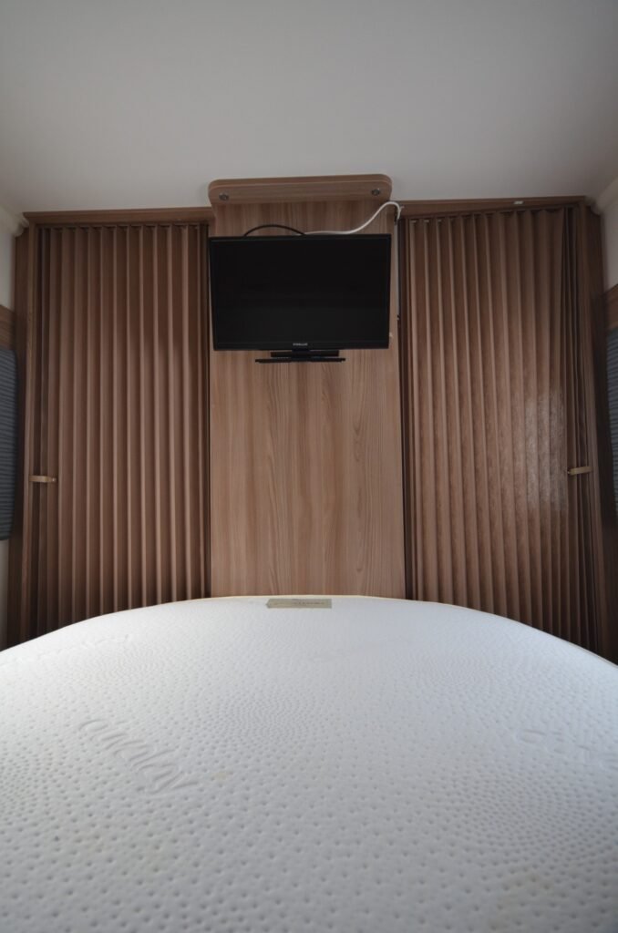 Obrázek interiéru obytného vozu s manželskou postelí a televizí. Komfortní a moderní design pro váš cestovatelský život.