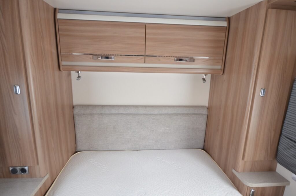 Obrázek zobrazuje útulný interiér obytného vozu s dřevěnými prvky a pohodlným lůžkem.