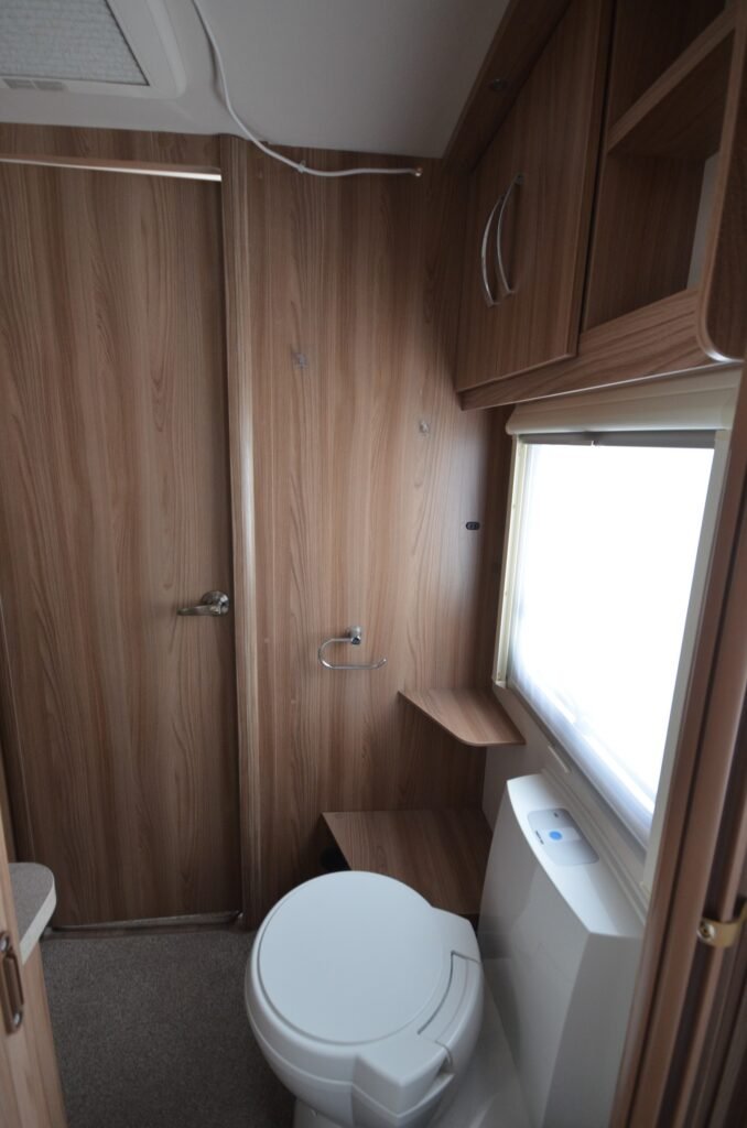 Koupelna v karavanu, moderní dispozice s dřevěnými akcenty a toaletou. Ideální pro pohodlné cestování.