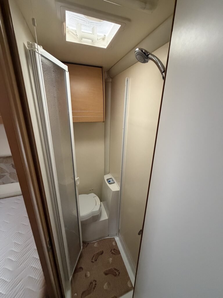 Interiér obytného vozu s koupelnou, sprchou a toaletou pro pohodlné cestování.
