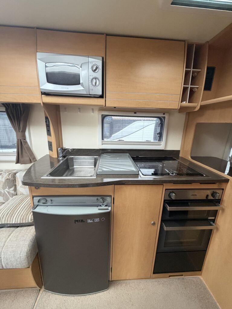 Kuchyňský kout v karavanu s mikrovlnkou, lednicí a sporákem. Moderní design a funkční uspořádání. Ideální na cestování.