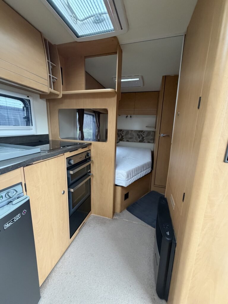 Interiér karavanu, obývací prostor s kuchyňskou linkou a spací zónou. Moderní a pohodlné uspořádání.