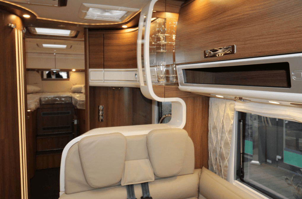 Interiér obytného auta s moderním designem a dřevěnými akcenty. Vybaveno pohodlným sezením a úložným prostorem.