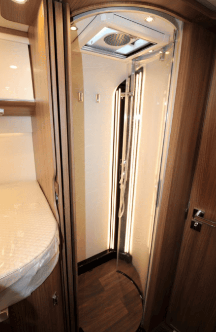 Obrázek interiéru obytného vozu se sprchovým koutem a moderním designem. Elegantní detaily pro pohodlí na cestách.