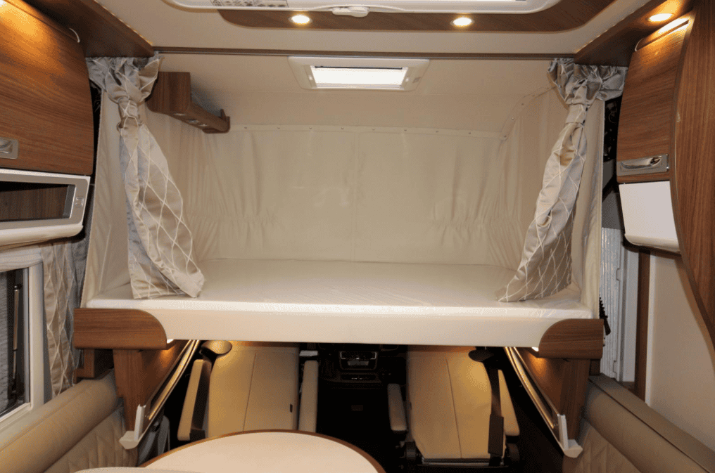 Obrázek interiéru obytného auta s prostorným rozkládacím lůžkem a elegantním dřevěným nábytkem.