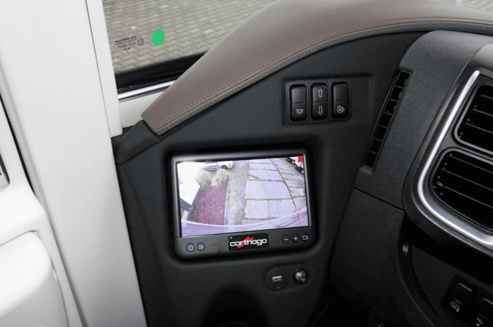 Obrázek interiéru obytného auta s kamerou a ovládacími prvky značky Carthago. Moderní technologie pro bezpečnost.
