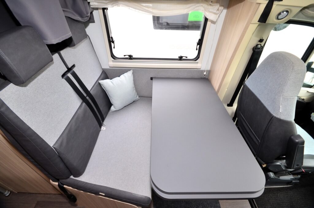 Interiér obytného auta s pohodlnou sedačkou, stolem a světlem. Ideální pro relaxaci a odpočinek na cestách.