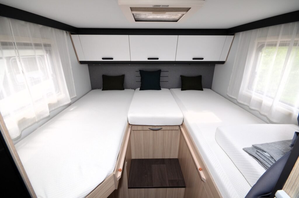 Obrázek interiéru obytného auta s prostornými lůžky a moderním designem, ideální pro pohodlné cestování.