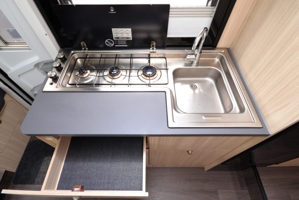 Moderní kuchyňka v obytném autě s dřezem a plynovými varnými hořáky. Praktické uspořádání pro kempování.