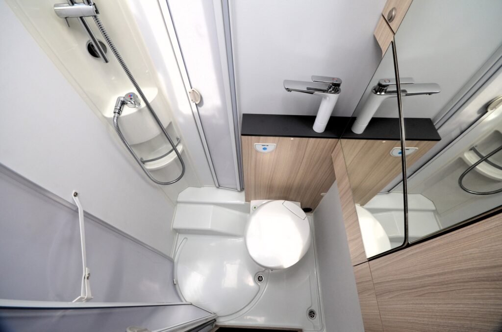 Koupelna s toaletou a sprchovým koutem v obytném voze, moderní design a praktické uspořádání.