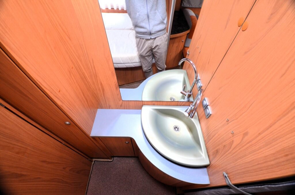 Obrázek interiéru karavanu s dvoulavou umyvadlovou částí a dřevěným obložením. Komfortní a praktický prostor.