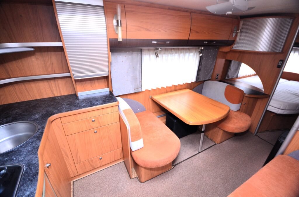 Interiér karavanu s dřevěným nábytkem, kuchyňkou a jídelním koutem. Stylový a pohodlný prostor pro cestování.