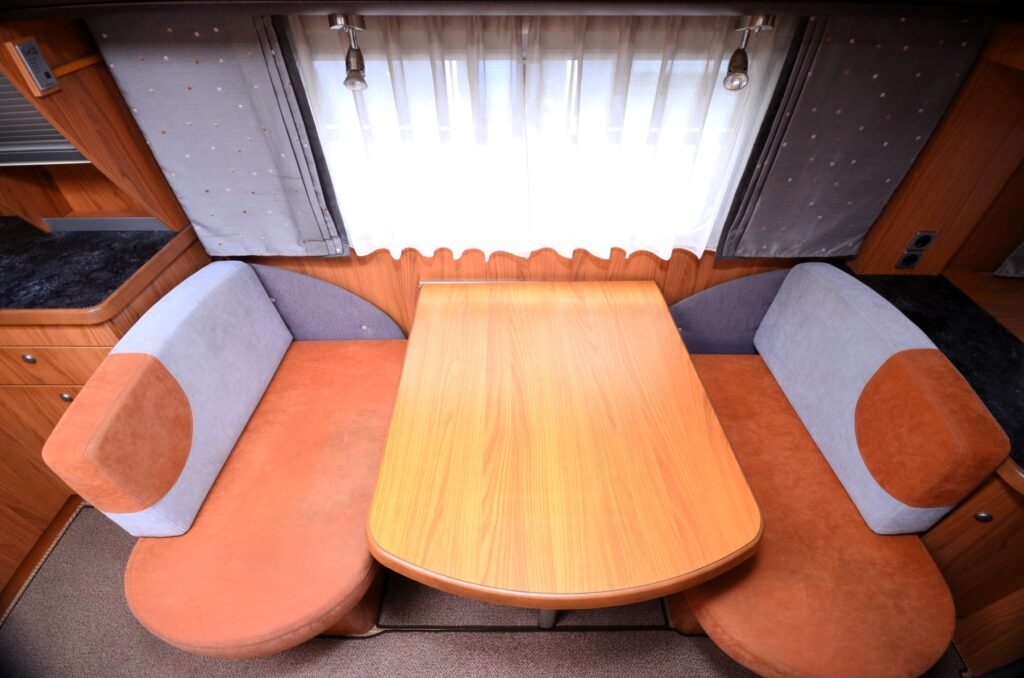 Obrázek interiéru karavanu s pohodlným sezením a dřevěným stolem pro relaxaci a stravování.