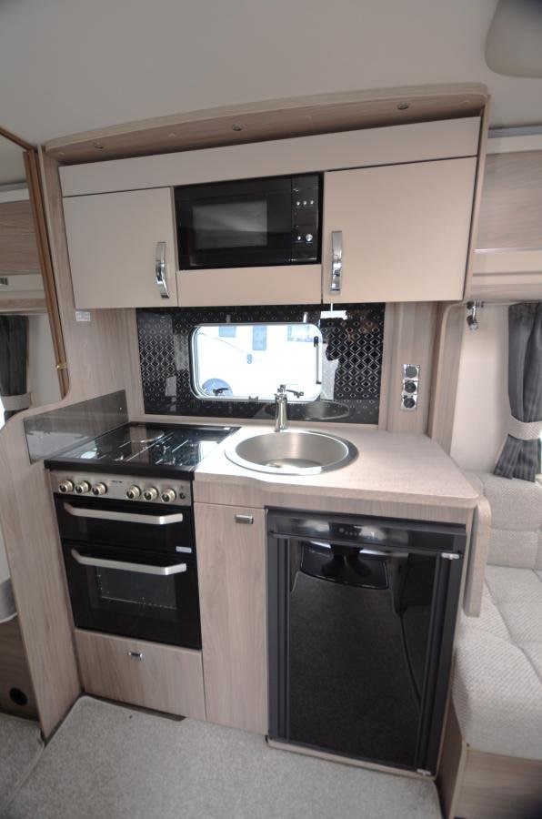 Obrázek interiéru moderního karavanu s kuchyňským koutem, dřezem a spotřebiči. Ideální pro cestování.