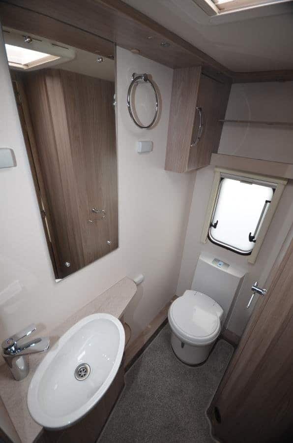 Obrázek interiéru karavanu s umyvadlem, zrcadlem a toaletou. Moderní design pro maximální pohodlí.