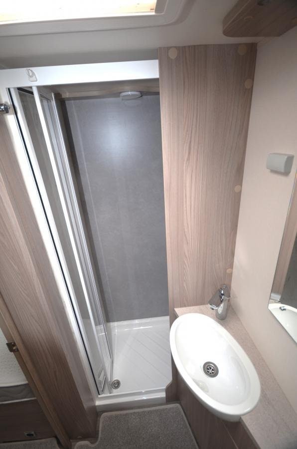 Obrázek interiéru karavanu, zahrnující sprchový kout a umyvadlo. Moderní design a funkčnost pro pohodlné cestování.