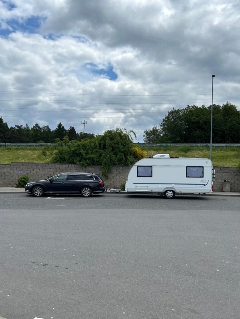 Na obrázku je karavan značky Adria, tažený černým autem. Ideální pro dovolenou a dobrodružství.