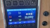 Ovládací panel obytného auta značky Hobby, se zobrazením funkcí a teploty. Moderní design pro pohodlné využití.