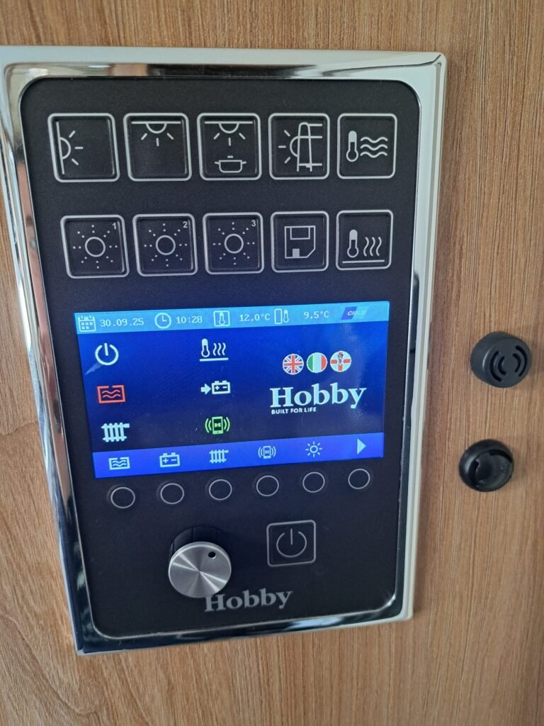 Ovládací panel obytného auta značky Hobby, se zobrazením funkcí a teploty. Moderní design pro pohodlné využití.