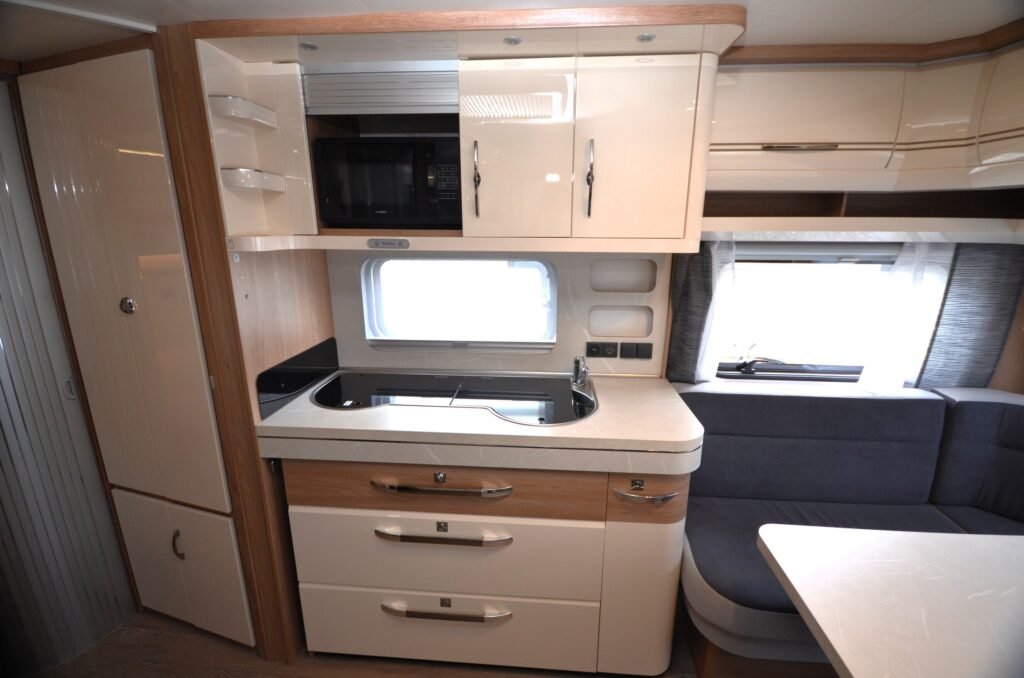 Obrázek interiéru karavanu s moderní kuchyní a příjemným posezením. Ideální pro relaxaci na cestách.