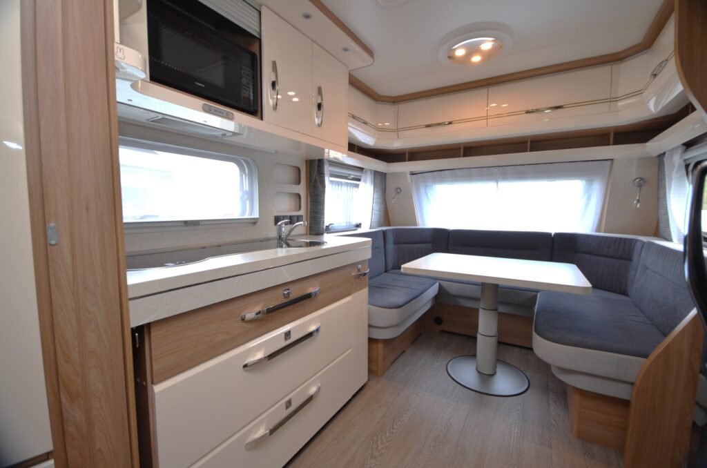 Obrázek interiéru karavanu s pohodlným sezením a kuchyňským koutem, ideální pro kempování a cestování.