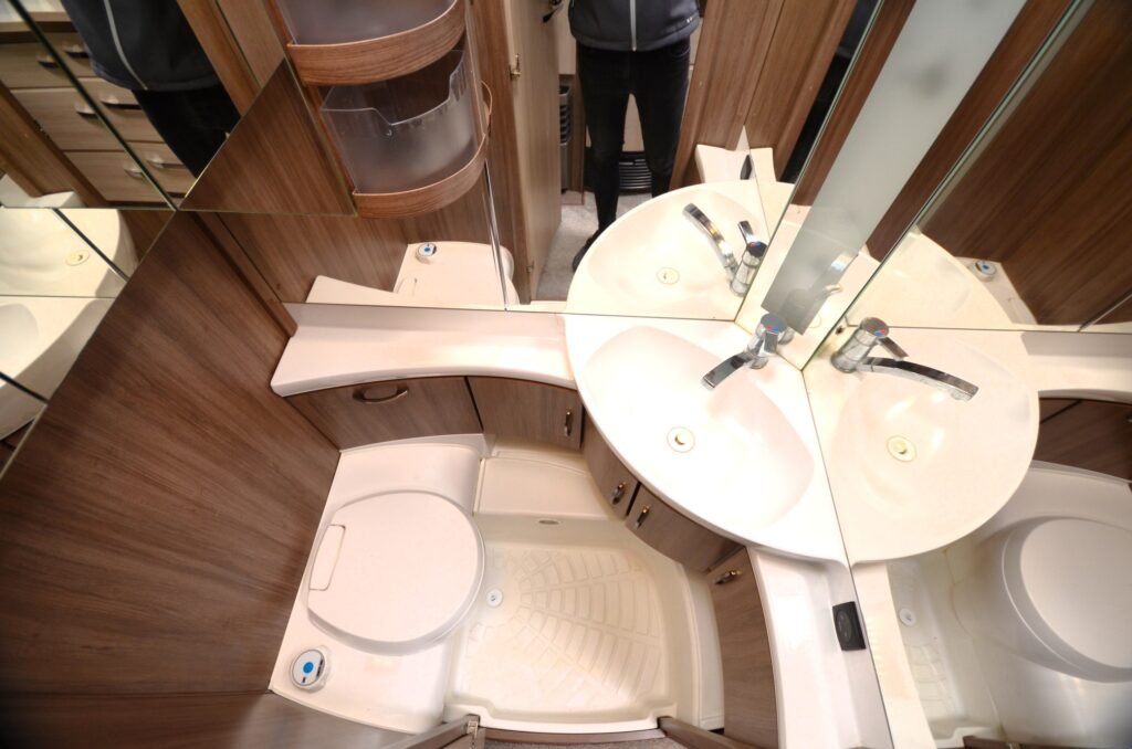 Koupelnový prostor s umyvadlem a toaletou v obytném autě. Moderní design a funkční uspořádání pro pohodlí na cestách.