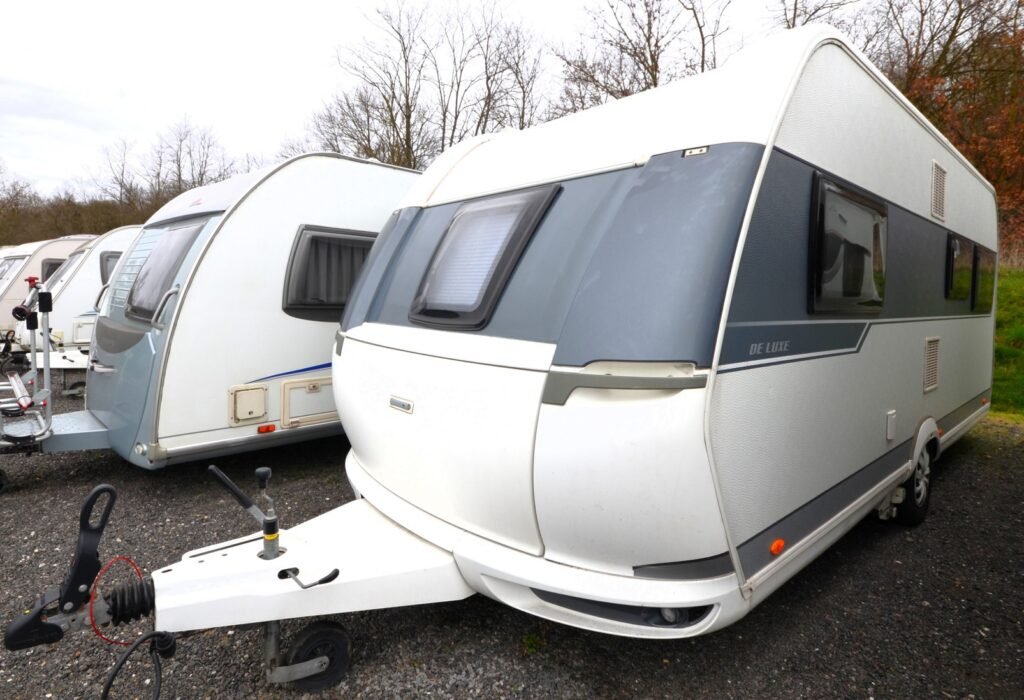 Karavan De Luxe stojí na parkovišti mezi dalšími modely, připraven na dobrodružství.