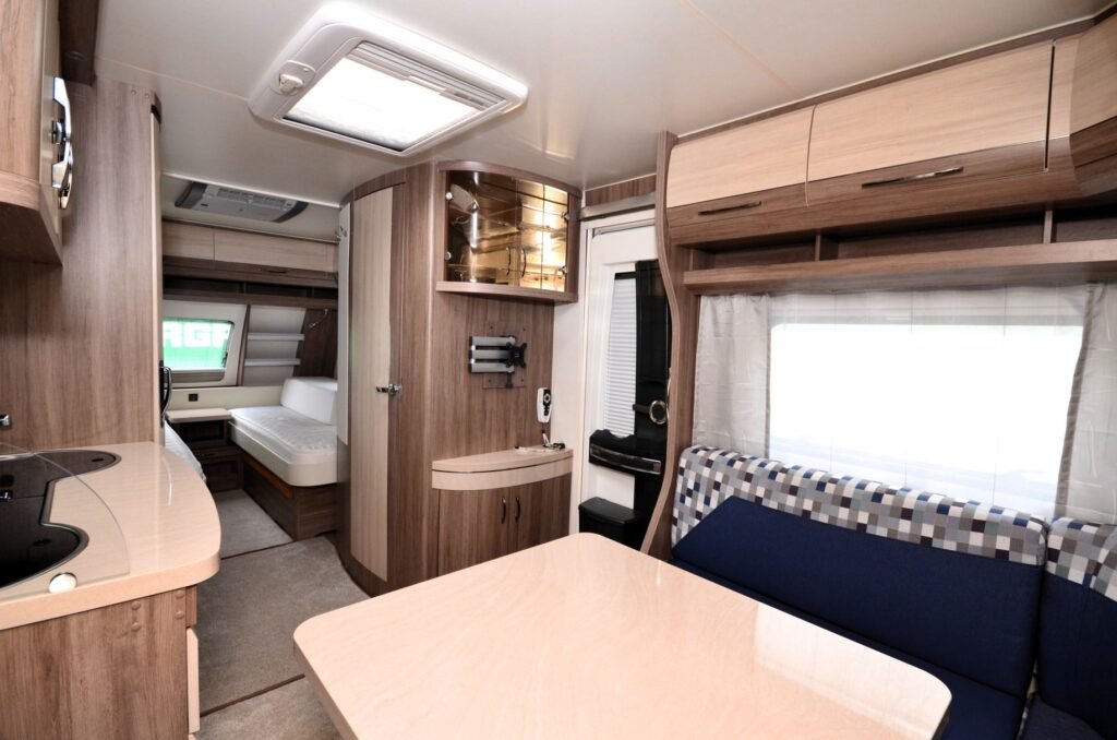 Interiér karavanu s moderním designem a dřevěnými prvky, zahrnující kuchyňku a pohodlné sezení.