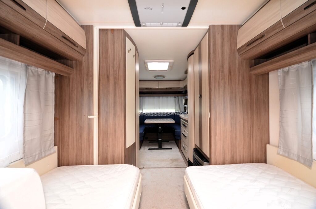 Interiér obytného auta s dvojlůžkem, jídelním koutem a kuchyní. Moderní design se dřevěným obložením.