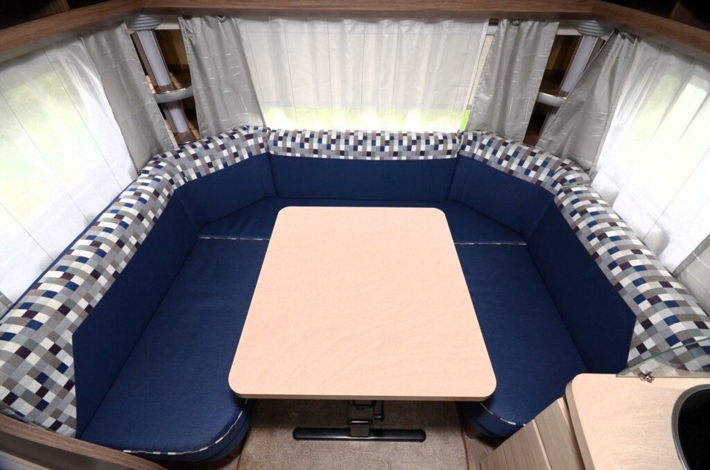 Obrázek zobrazuje útulný interiér karavanu s modrými sedáky a stolečkem. Ideální pro rodinné chvíle.