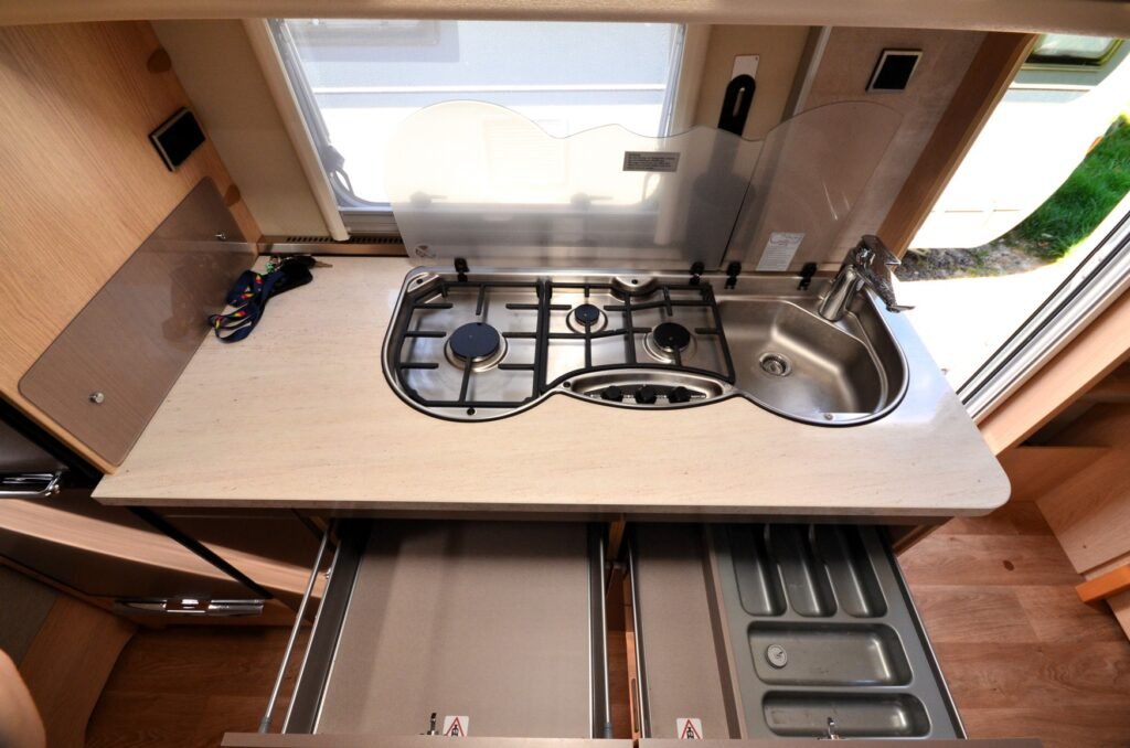 Kuchyňka v karavanu s plynovým vařičem a dřezem, ideální pro pohodlné vaření na cestách.