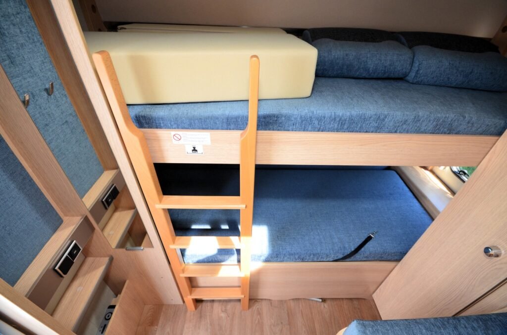 Obrázek interiéru obytného auta s patrovou postelí a modrými sedáky pro pohodlné spaní.