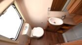 Obrázek interiéru karavanu s toaletou a umyvadlem. Elegantní design a praktické úložné prostory.